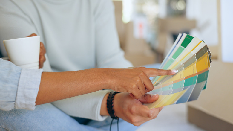 People holding color swatches, coffee mug in one hand.
