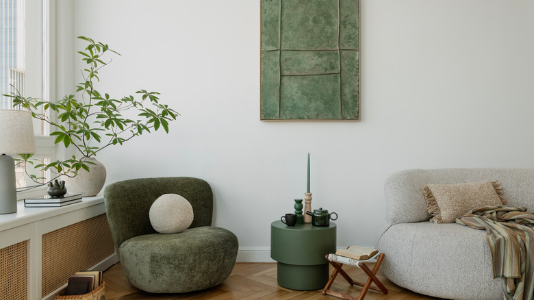 A living room with green accent furniture, chair, circular end table, and jade green artwork