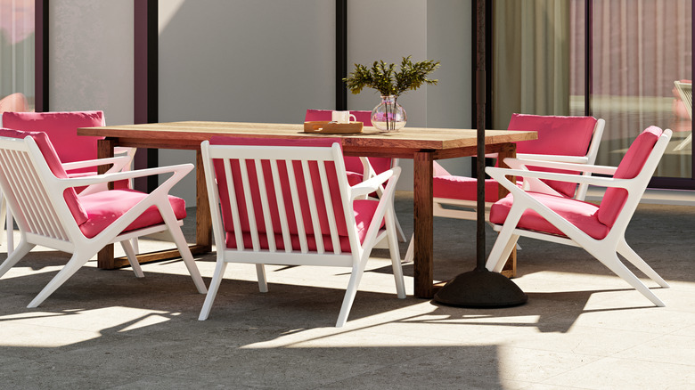 White chairs with pink cushions surround a wooden table on an outdoor patio