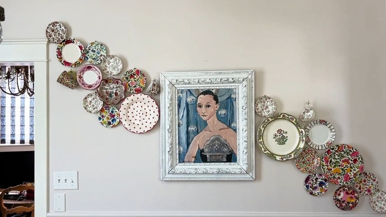 Various patterned plates hung on wall around a framed painting.