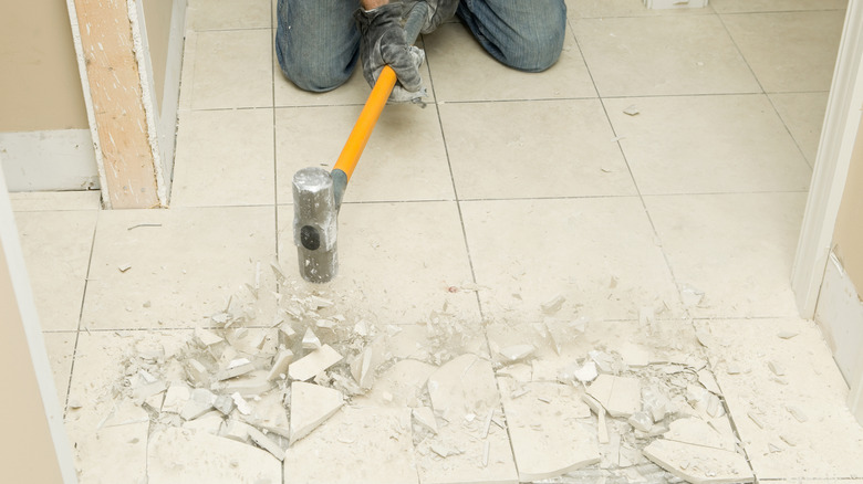 Man using sledgehammer to break up floor tiles.