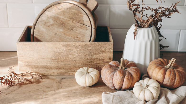 Pumpkins in muted colors and dried plants in a vase in front of a wood box in the kitchen