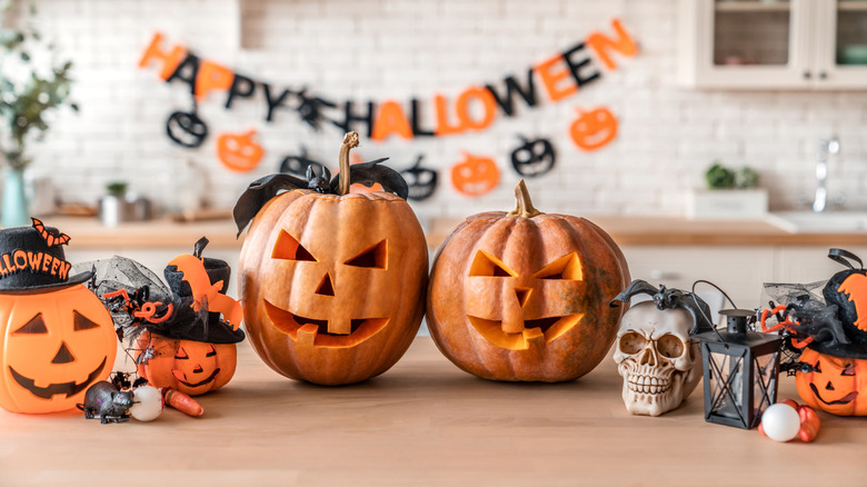 A kitchen with a Happy Halloween banner in the background and pumpkins, rats, skulls, and spiders in a row in the foreground