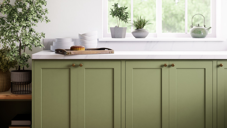 Dill cabinetry below a white countertop within a bright, airy kitchen.