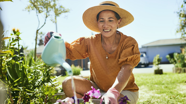 A woman using a watering can to water flowers