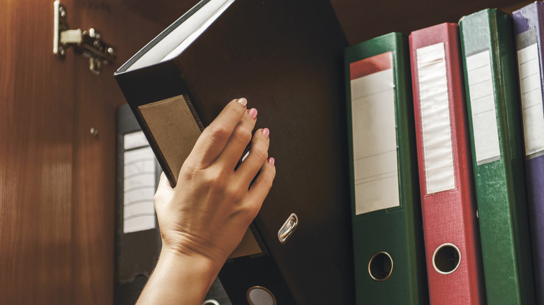 A hand pulling a big black binder off a shelf in a cabinet