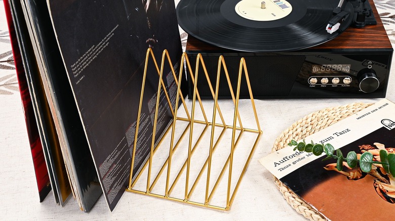 Vinyl records sit in a triangular gold-finished metal holder next to a record player.
