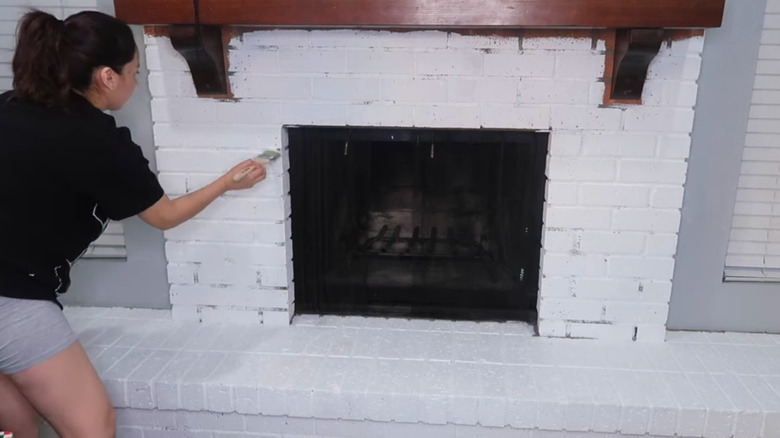 A person paints the brick fireplace white