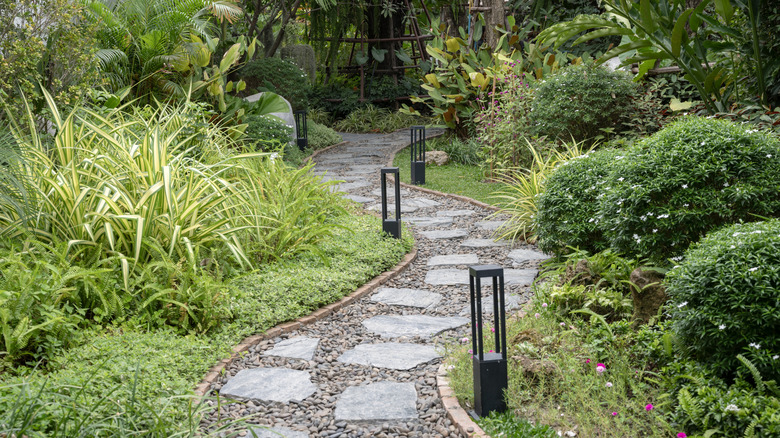 A pathway cuts through a garden, made from slabs of flat cobblestone that are set within gravel.
