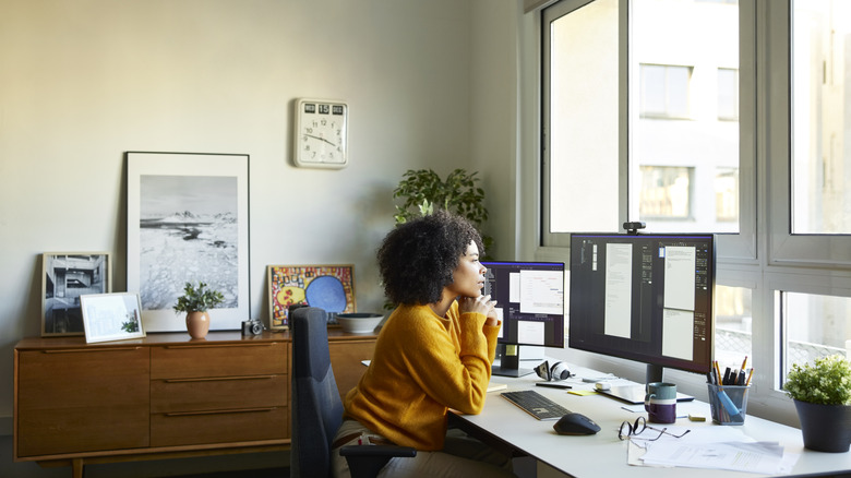 A woman peering out a window in her home office