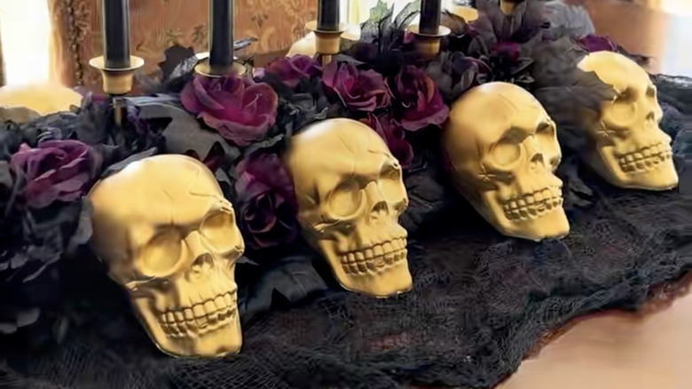 A completed DIY Halloween table decor piece with gold skulls, black candles, and dark florals