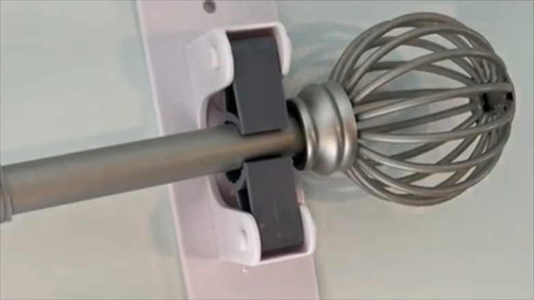 A curtain rod with a finial is stuck to a wall with a Dollar Tree broom hanger.