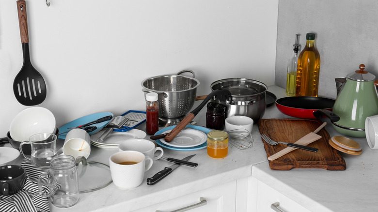 Cluttered kitchen countertop with plates, cups, and cutlery