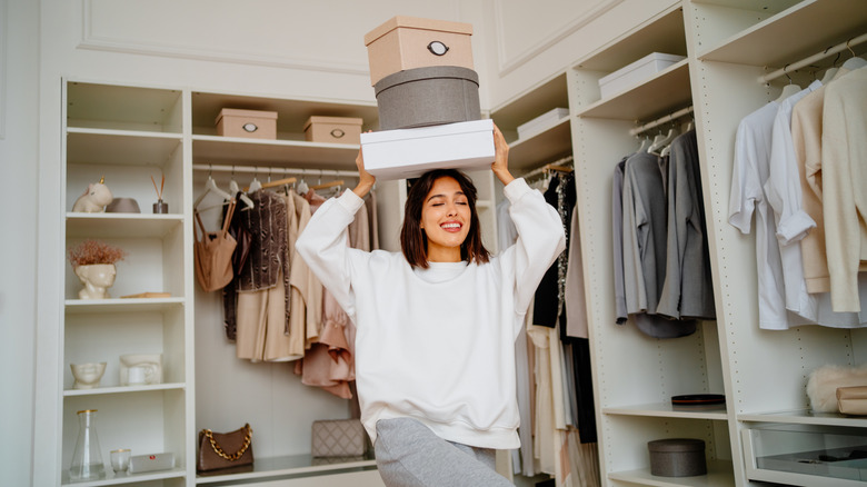 Smiling lady in her closet holding storage bins above her head.