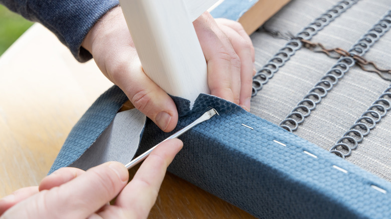 A man taking staples from a chair's blue fabric with a flathead screwdriver.