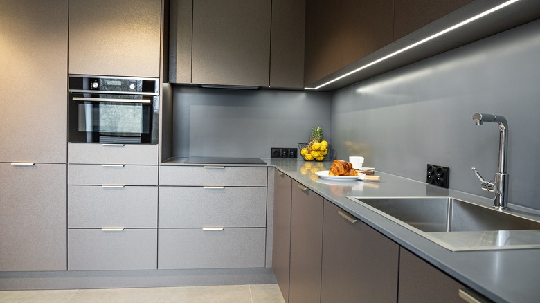 A modern kitchen with linear lighting under the cabinets and a sleek, plain grey backsplash.