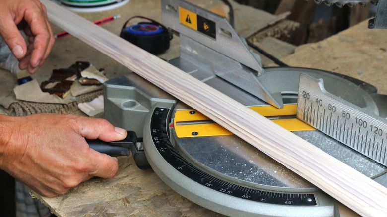person adjusting miter saw with piece of wall trim on it
