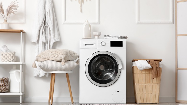 A washing machine with detergent on top next to laundry basket