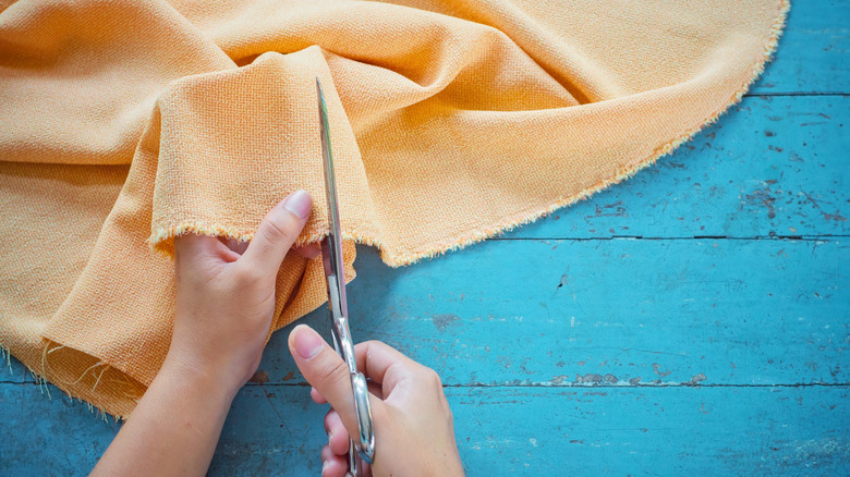 hands holding and cutting orange cloth fabric with scissors.