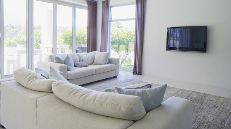 Open living room with couches, rug, TV on the wall, and windows with open curtains