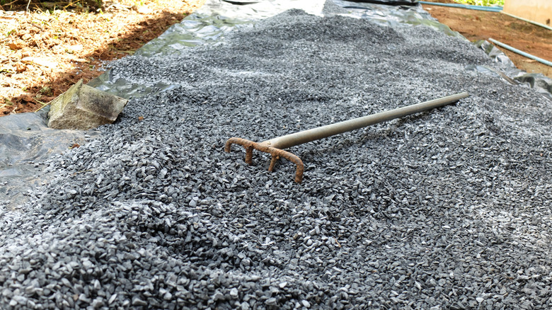 Gravel being installed on top of black plastic sheets with a stone rake.