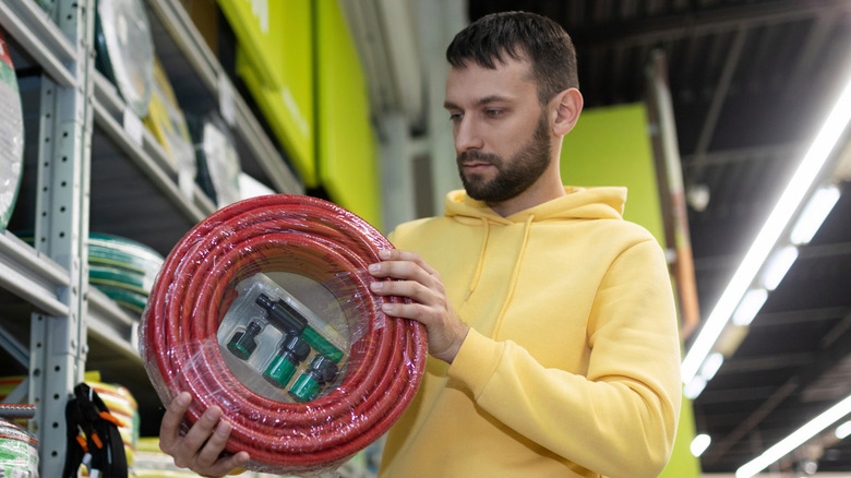 A man picking up and inspected a garden hose in a hardware store.