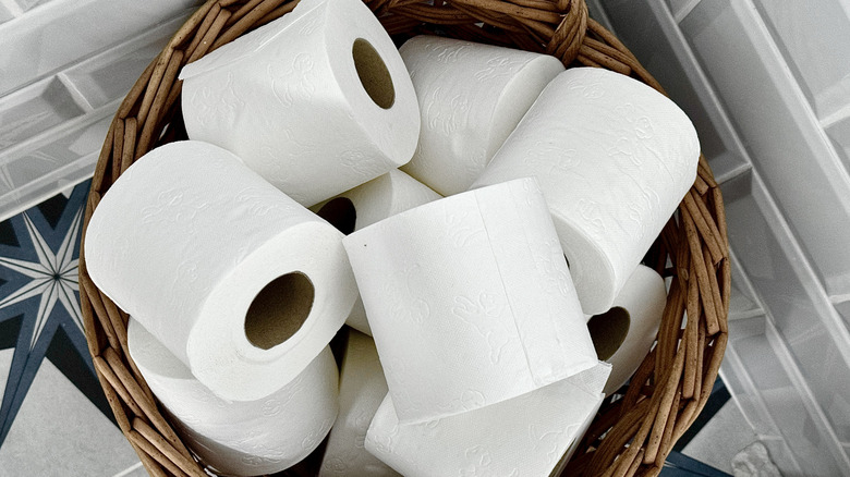 A basket of toilet paper rolls on the floor of a bathroom