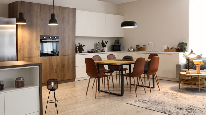 Interior of modern open plan kitchen with dining table, white oak floors, and glowing lamps