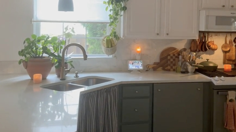 Cabinet with a curtain covering it, below a kitchen window