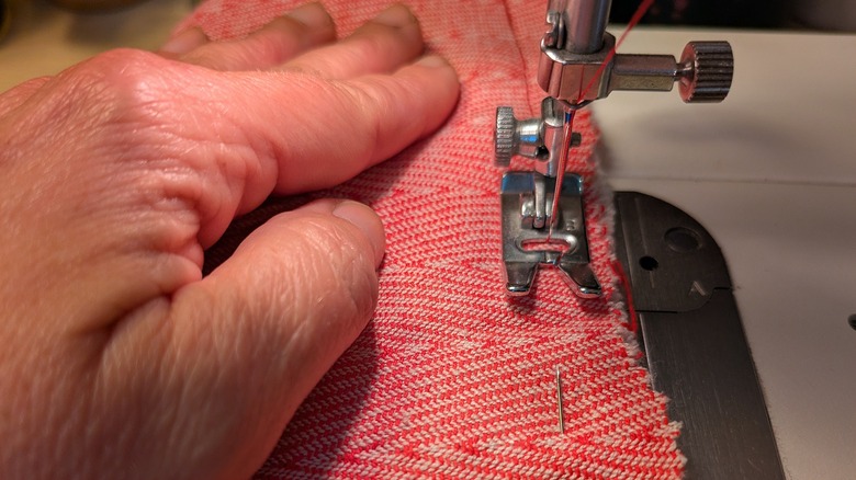 One hand guides pinned red fabric through a sewing machine.