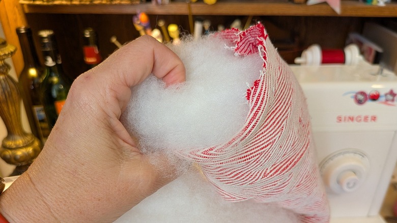 One hand fills a red and white fabric tube with polyester stuffing.