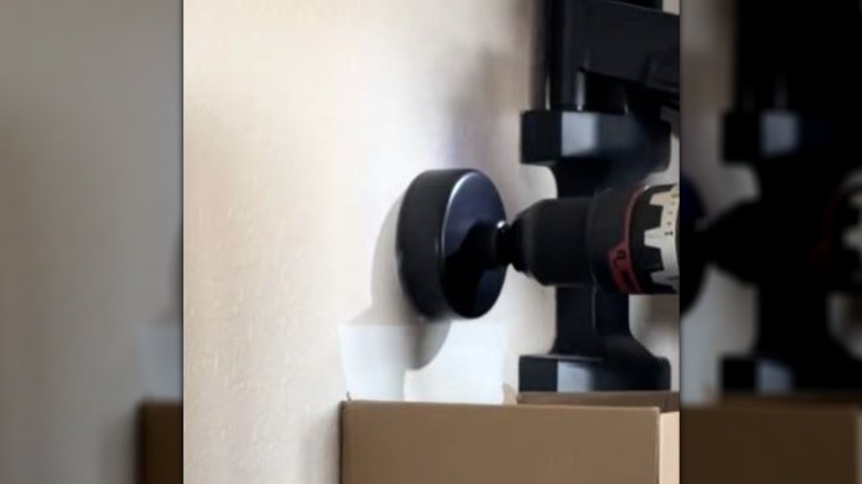 A cardboard delivery box is taped to drywall beneath a power drill.
