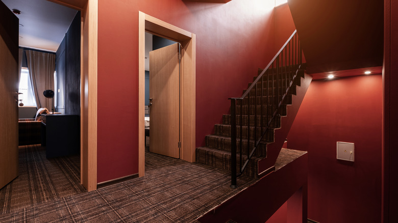 The start of a hallway off stairs with dark carpet, jewel toned walls, and overhead lighting.