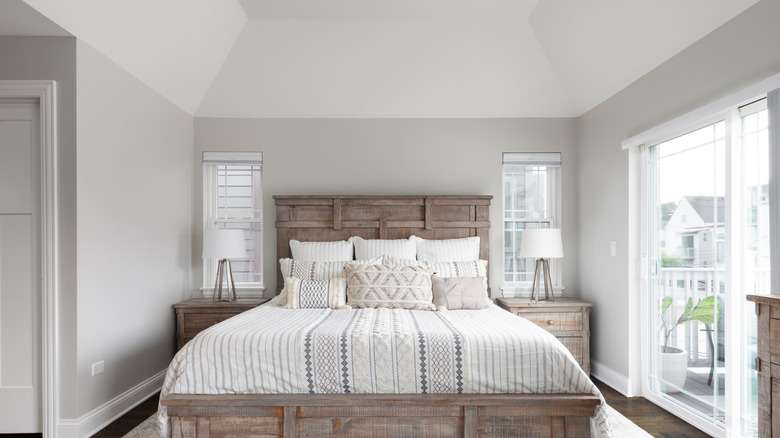 Modern white bedroom with bright natural light, wooden bed frame, and multiple bed pillows.