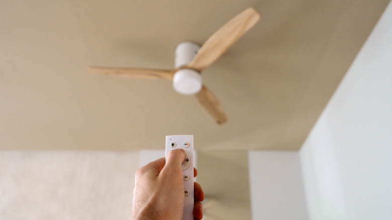 A man pointing a remote control at a bedroom ceiling fan.