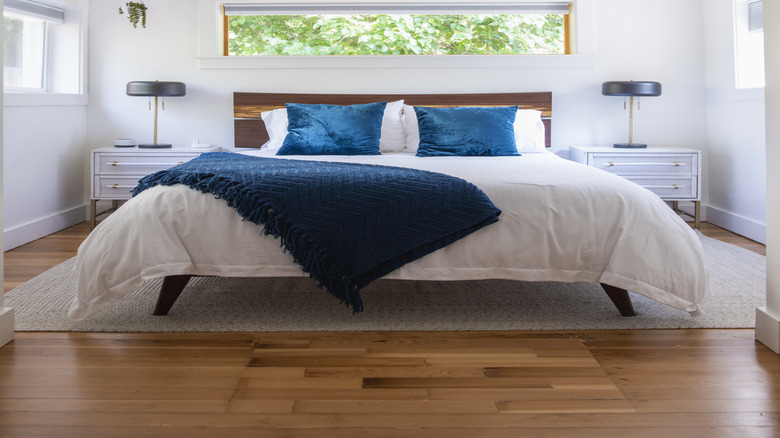 A ceiling fan spinning above a bed with long rectangular window and white walls.