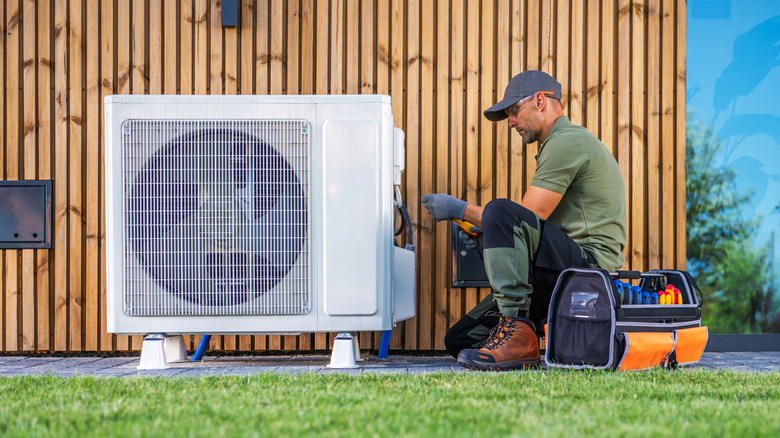Repair man works on a broken central air conditioning unit outside of home.