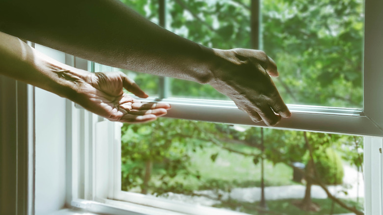 A close up of a person's hands opening a window from the bottom