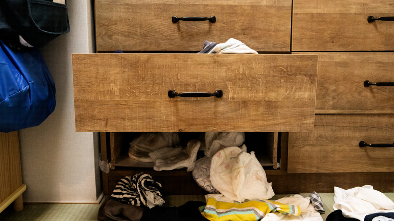 wood dresser with broken bottom drawer and clothes hanging out