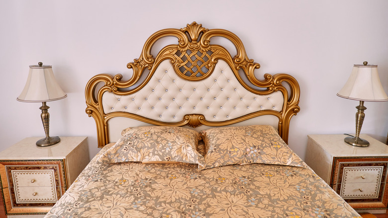 Close-up of antique-style gold bed frame with intricate headboard, two bedside tables, and lamps