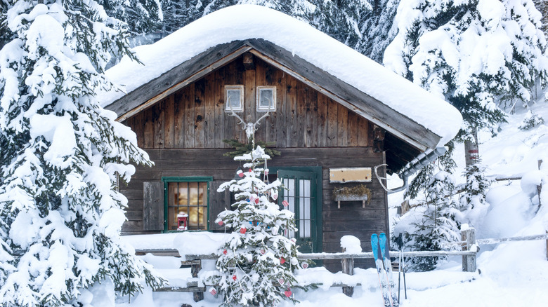 A wooden winter cabin in the mountains is covered in snow.