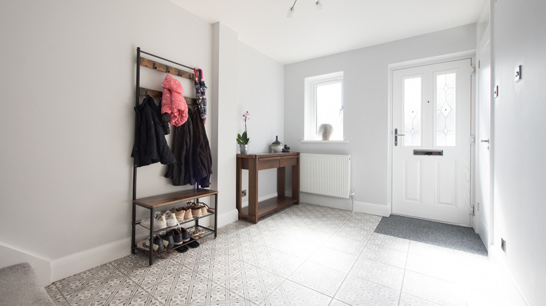 A modern, white entryway with a minimalist shoe rack unit and a wooden sideboard.