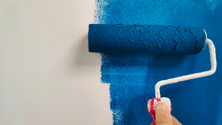 A close up of someone using a paint roller to apply blue paint to a white background.