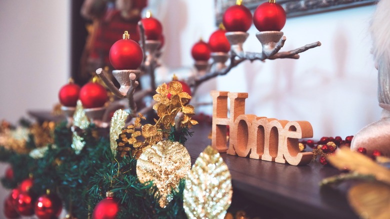 Red and green Christmas decor on mantel with "Home" tabletop sign