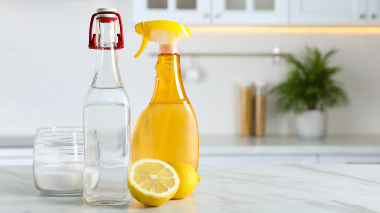 Vinegar, baking soda and lemon on white marble table in kitchen, space for text. Eco friendly natural detergents