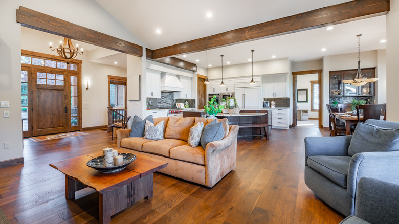 Open concept living room, kitchen and dining room with exposed beams, and natural wood front door with glass