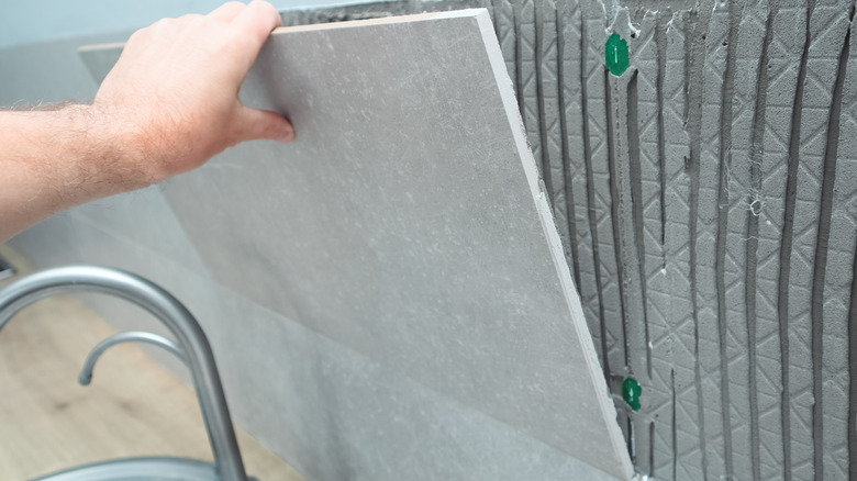 A man removing a large backsplash tile from grout