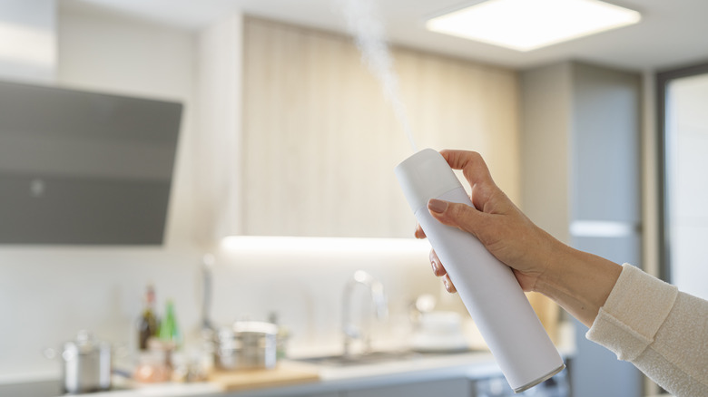 A hand spraying a bottle of air freshener in a kitchen