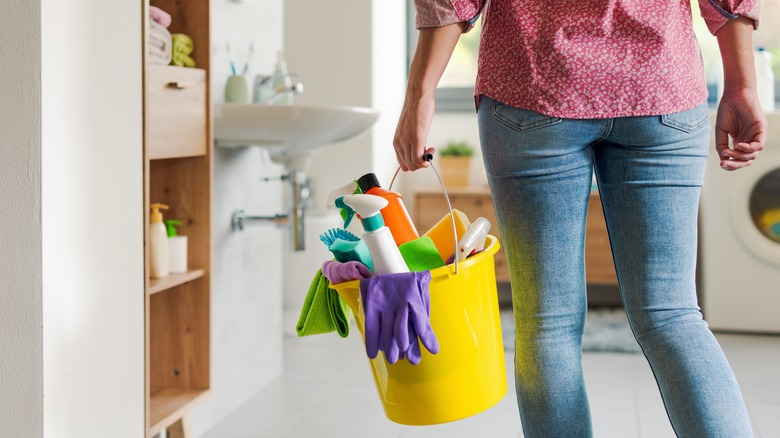 Person holding a yellow bucket with cleaning products