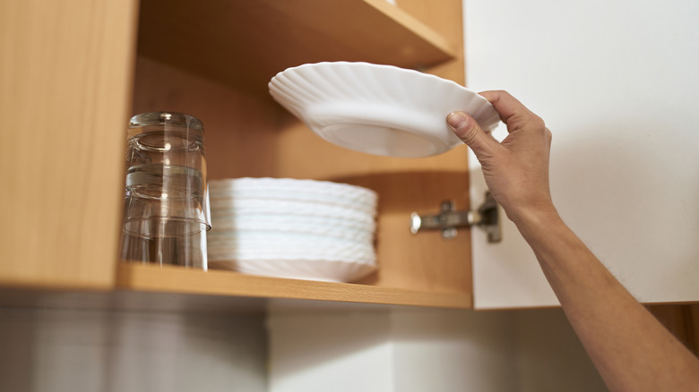 person taking out white china plate from cupboard